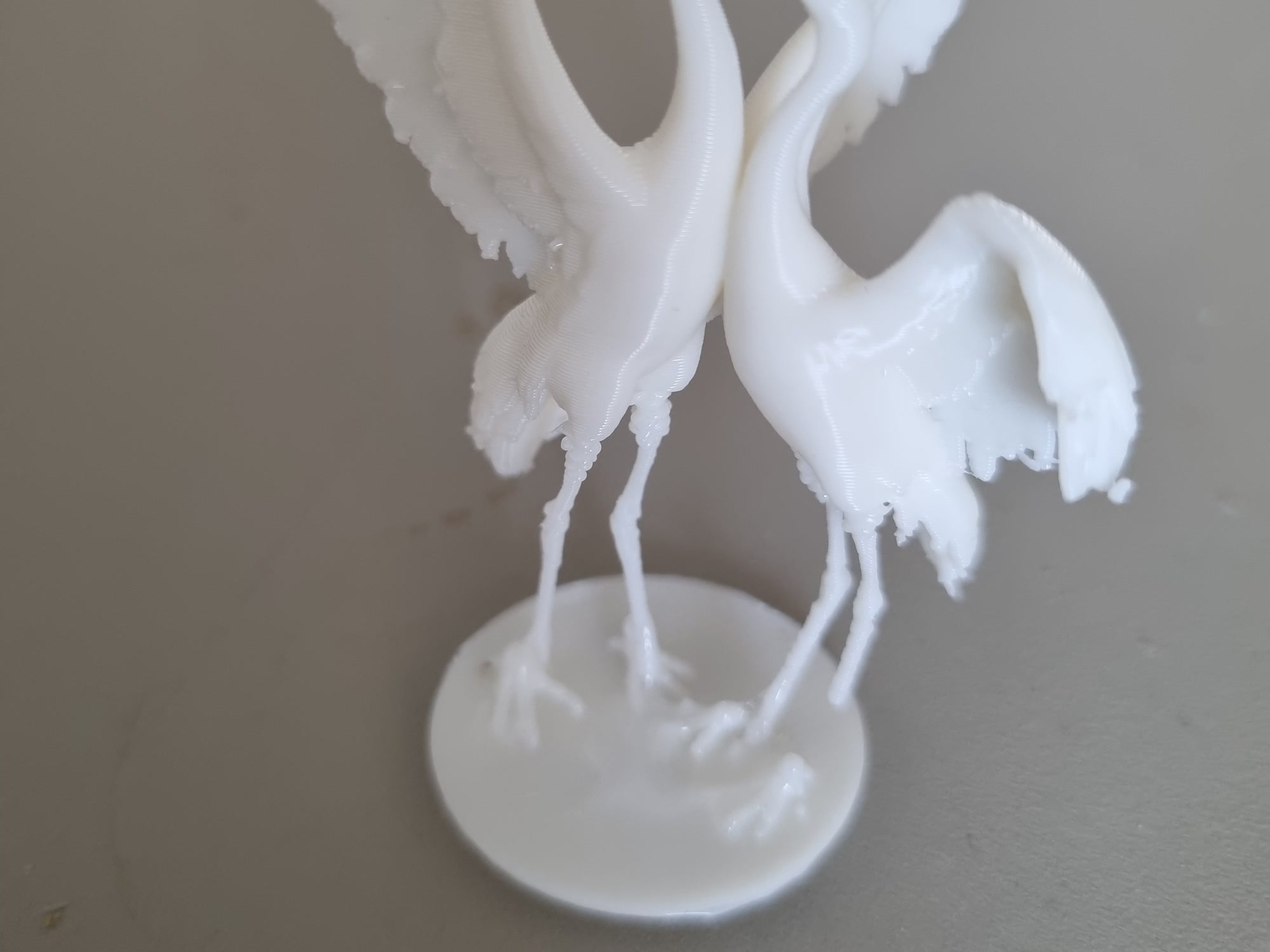 Two white 3D printed brolgas dancing on a round base, wings lifted