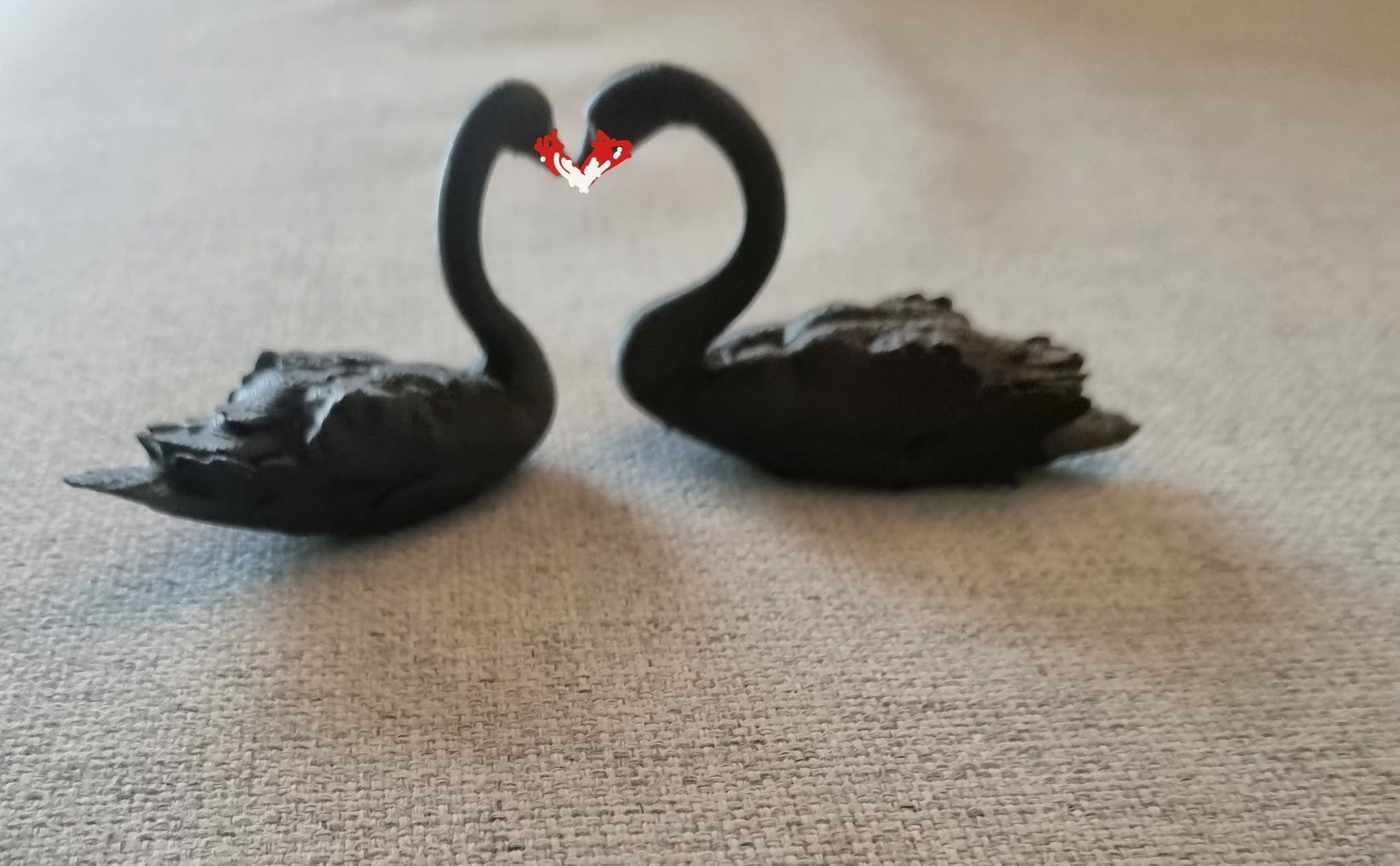 Two black 3D printed swans facing each other, their necks making a heart shape