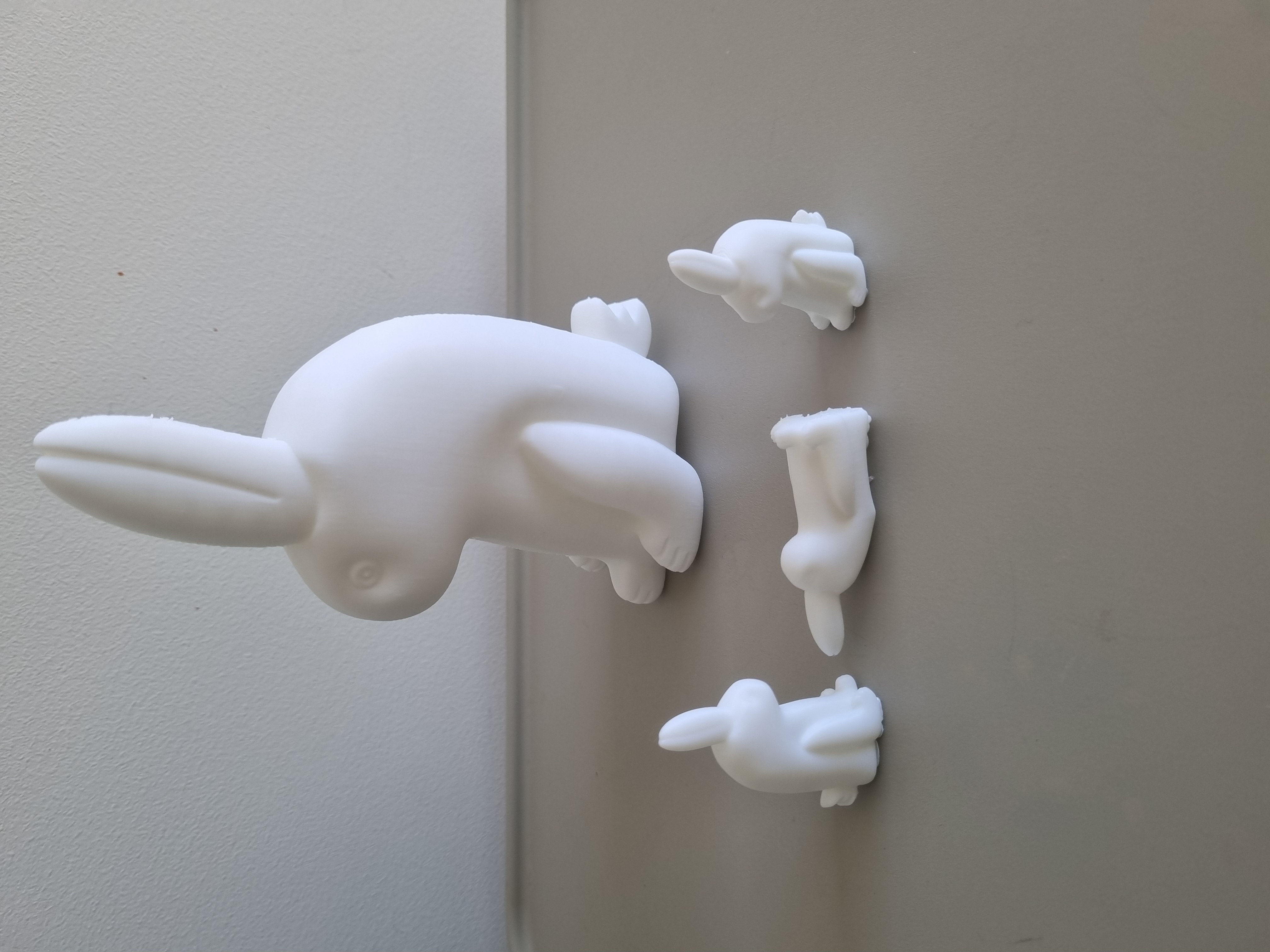 One large white 3D printed rabbit with three tiny rabbits in front of it