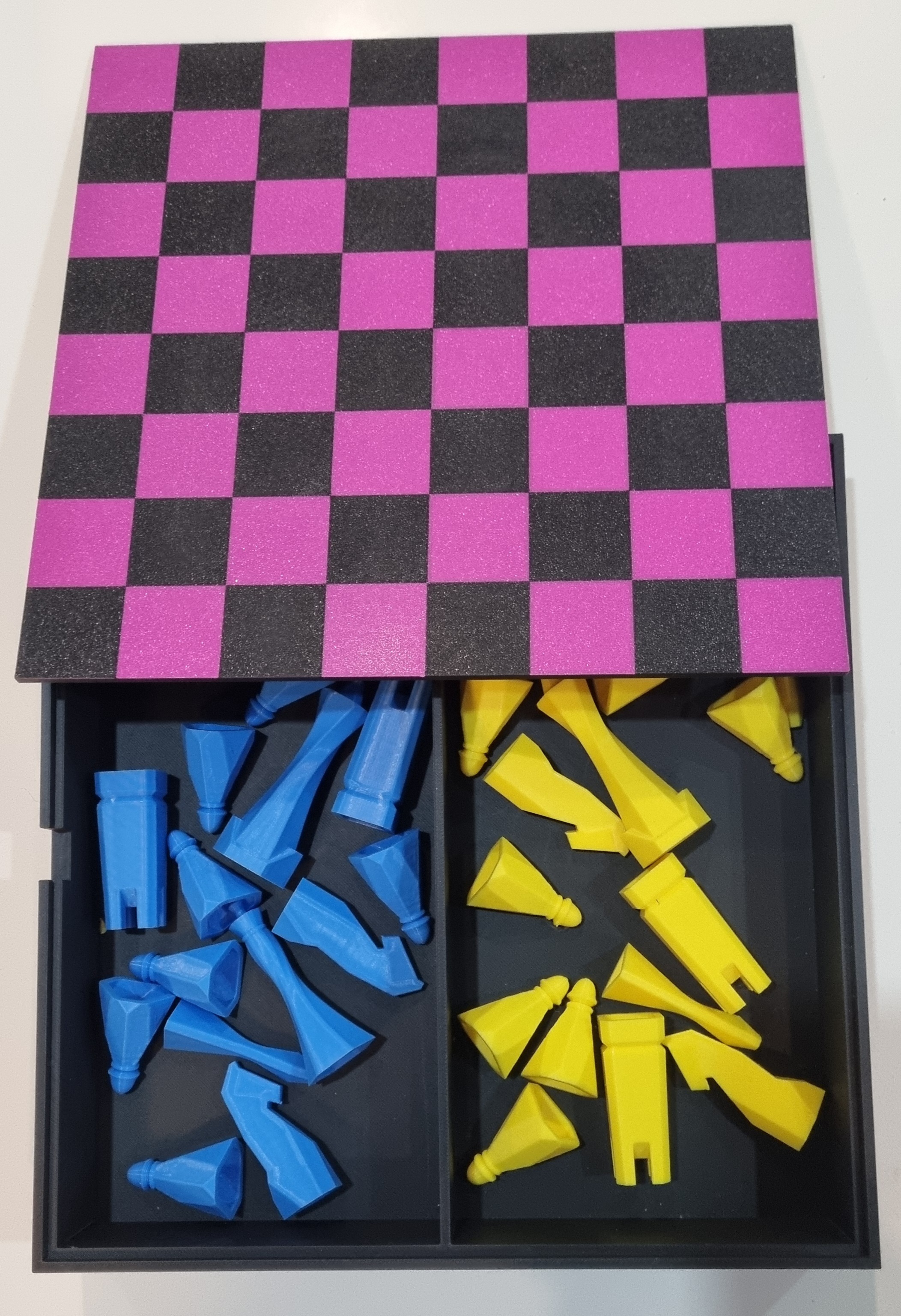 A pink and grey 3D printed chess board that opens as a box, with blue and yellow pieces inside