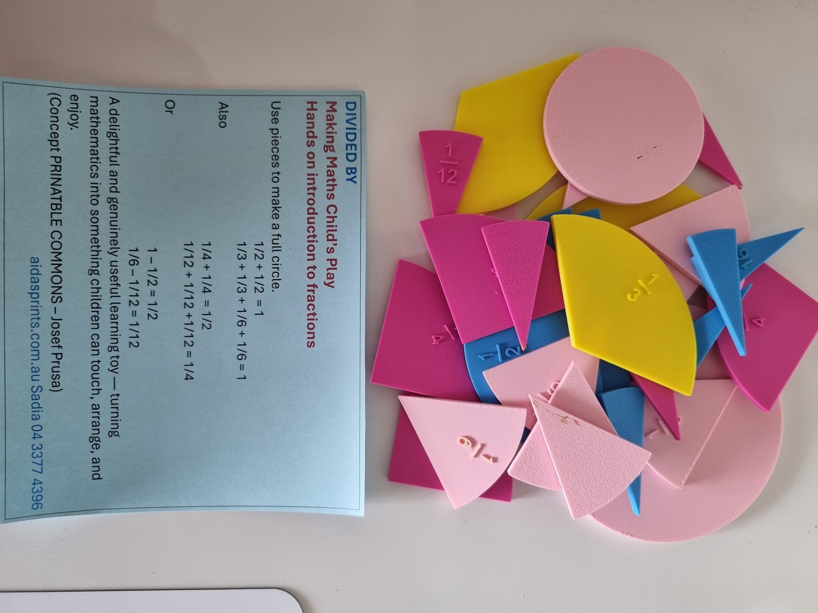 A pile of pink, yellow and blue fraction pieces, including halves, thirds, quarters and twelfths, next to a Divided By card