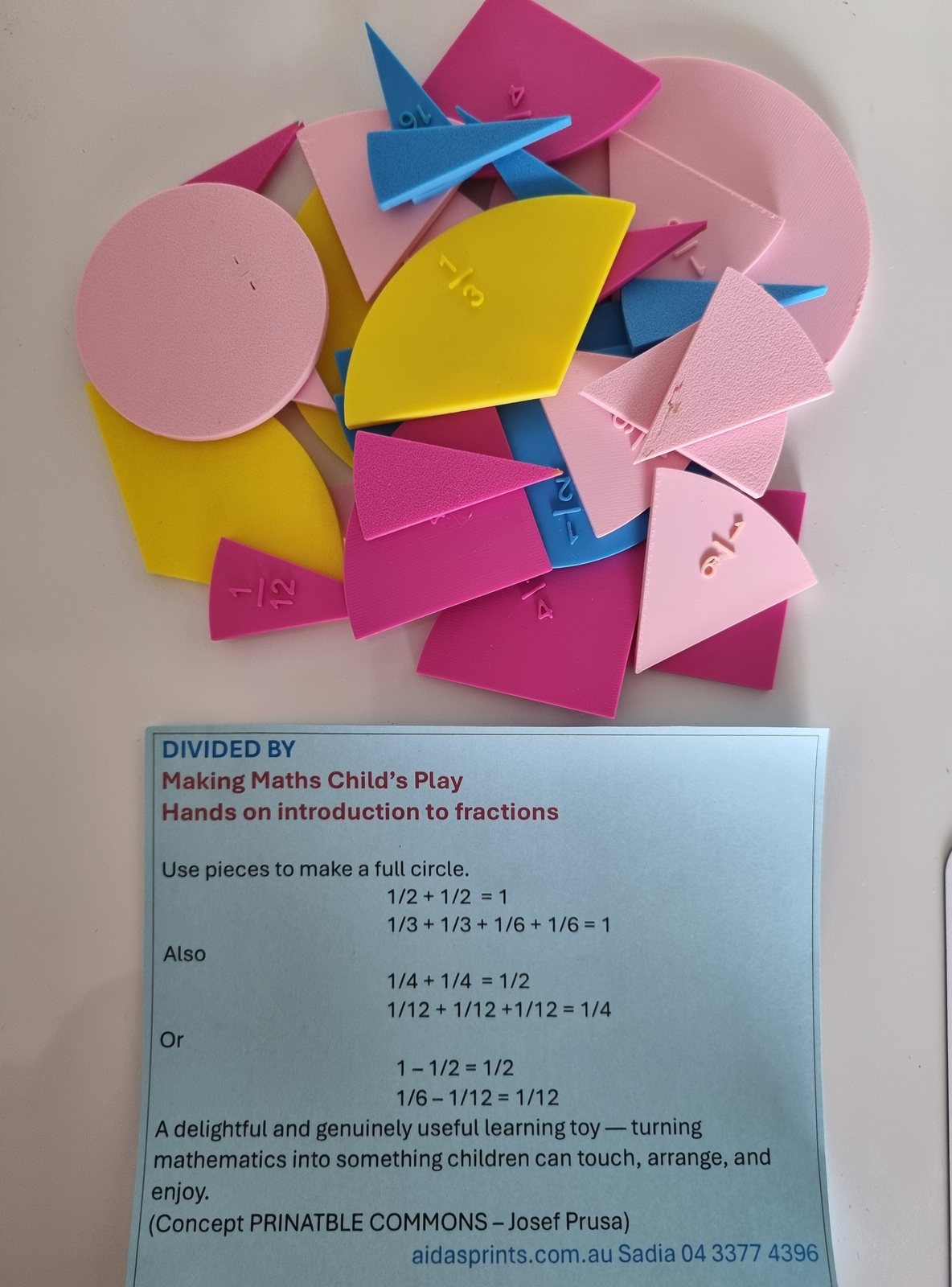 Colourful 3D printed fraction pieces in pink, yellow and blue, above a Divided By card