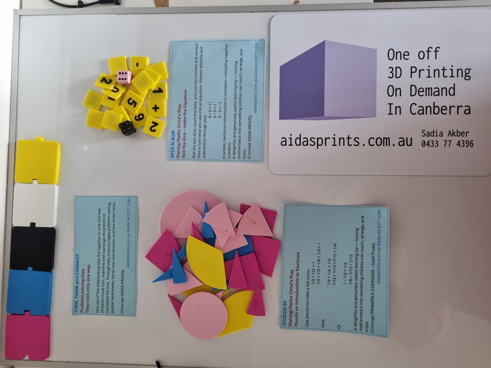 Three learning games on a white board: fraction pieces, yellow number tiles with dice, and five coloured interlocking tiles, with an Aidas Prints card