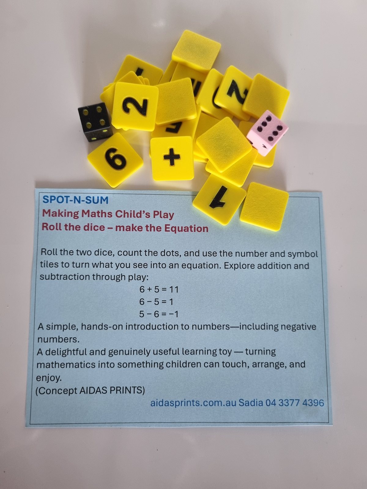 Soft yellow number and symbol tiles, with a black die and a pink die, above a Spot-N-Sum card